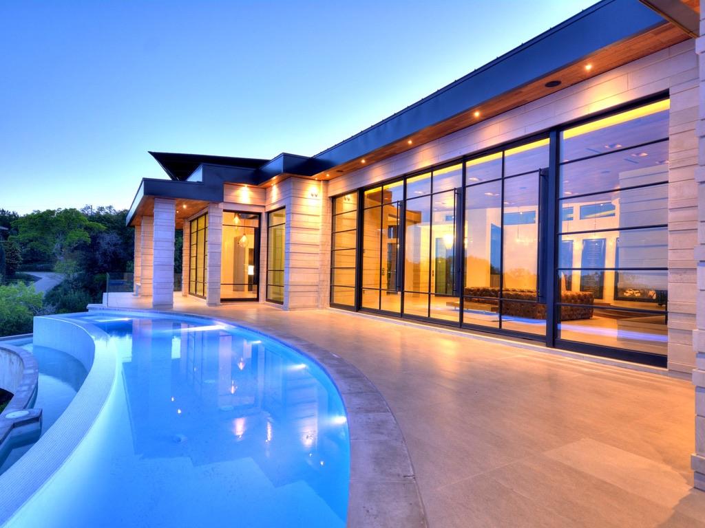 Black steel window wall along a pool terrace at dusk